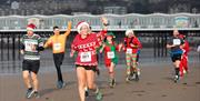 A group of runners in Christmas jumpers and festive hats wave to the crowds as they take part in the Weston-super-Mare Christmas Cracker race on the t
