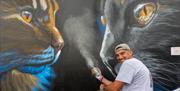 A street artist with spray can working on his giant cat mural at the Weston Wallz Spray Jam in the Italian Gardens Weston-super-Mare