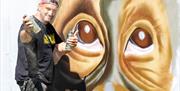 A street artist with spray can working on a giant mural of a monkey