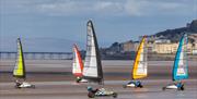 Five Blokarts with their colourful high sails racing across the sandy beach at Weston-super-Mare