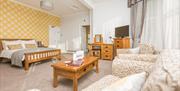 A double room with yellow wallpaper on wall behind the bed,, a coffee table and comfy chairs