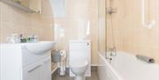 A bathroom with vanity sink, loo and bath with shower over