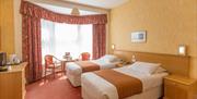 A twin bedded room with long, pink patterned curtains and yellow walls