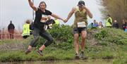 Two competitors in an endurance race jump together above a water pit