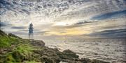 A distinctive lighthouse sitting on rocks beneath a sunset