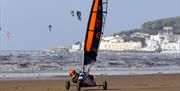 A land yachting racer racing across a beach with kite surfers in the background