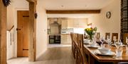 Open plan view through a dining room, which features a large dining table set for a meal, to the kitchen of a country cottage at Webbington Farm Cotta