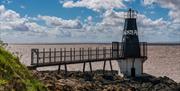 An odd-shaped short black lighthouse sitting on rocks overlooking the sea