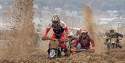 Sand flies up as three motorbike riders struggle through sand in a beach race