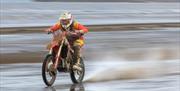 A racing motorcyclist in red racing across the shoreline of a beach