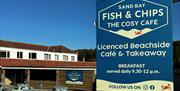 Close up image of the Sand Bay Fish & Chip shop sign against a blue sky with the premises in the background