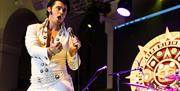 An Elvis impersonator, dressed in a traditional white Elvis suit, in full flow performing at the Harbor Lights Elvis Festival in Weston-super-Mare