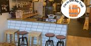 An empty bar counter with white tiles and five assorted stools in front of it