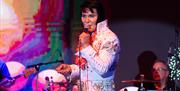 An Elvis impersonator dressed in the iconic white Elvis suit on stage and performing at the annual Harbor Lights Elvis Festival in Weston-super-Mare