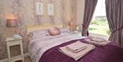 Double room with purple counterpane on bed and lilac curtains with lilac and cream wallpaper