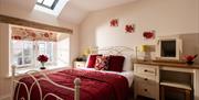 A luxury double bedroom at Webbington Farm Cottages, near Weston-super--super- Mare. The metal bed has a red duvet matching the blinds and wall art in