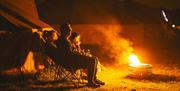 A family sitting on deckchairs outside their tent warming themselves in the glow of a campfire