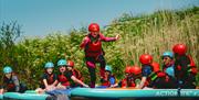 A child in a red helmet and lifejacket running across paddleboards on a river being watched by lots of other children on paddle boards at the Mendip A