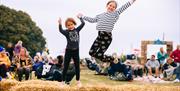 Two girls jumping over a bale of straw at the Mendip Family Festival