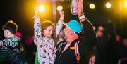 A dad holding a can of drink about to high five his young daughter during a night time concert at the Mendip Family Festival
