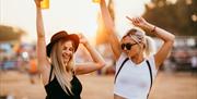 Two women dancing at an outdoor music festival both raising their pint glasses in the air