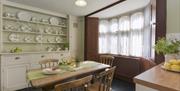 Period Victorian dining room with table and white dresser showing plates as well as a large curtained window