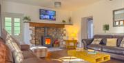 Interior of a large beamed lounge which features a glowing woodburner in an inglenook fireplace at Norton Court Farm Holiday Cottages at Sand Bay, Wes