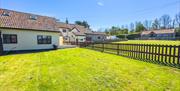 A large lawn and brown picket fence lead to a cream bungalow with red roof tiles at Norton Court Farm self-catering holiday cottages at Sand Bay, near