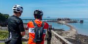 Two cyclists leaning against a fence admiring a sea view