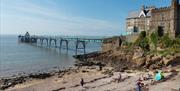 A pier emerging from a large rock on a shingle beach and jutting out into the sea