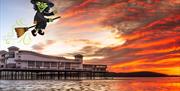 A cartoon-style witch flying off on her broomstick over Weston's Grand Pier and into the sunset