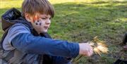 A boy with a football face paint design on his cheek creates a large spark as he uses flint to start a fire during an activity session at the Old Town