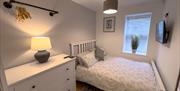 Light grey double bedroom with a white cupboard with a wardrobe rail above it inside the Seaside Apartments, Weston-super-Mare. There's a television o