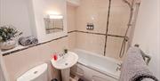 Magnolia painted and light brown tiled bathroom inside the Seaside Apartments, Weston-super-Mare. The room is adorned with grey towels and a pot of fl