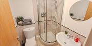 Shower room with a white toilet and sink as well as a round mirror on the wall at the Seaside apartments, Weston-super-Mare