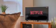 A large television displaying the word Netflix sitting on a wooden unit by a window with white blinds inside the Seaside Apartments, Weston-super-Mare