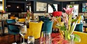 A dining room set for dinner with flowers on the table and blue and yellow chairs