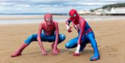 Two characters dressed as Spiderman in a crouched down Spiderman pose on Weston-super-Mare beach