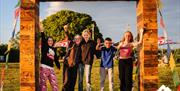 Five kids smiling and posing with hands up in the hand, stood on Mendip Basecamp's giant wooden frame with pray flags tied from frame to the ground. P