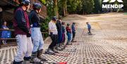 Image showers 7 people wearing skis and helmets on Mendip Activity Centre's artificial dry slope. Watching instructor further up the slope, walking up