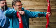 Side profile, close up photo of a man pulling back his bow and arrow, and looking down the arrow.