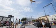 An acrobat high in the blue sky above the crowds and some apparatus