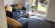 A lounge with grey seating and yellow cushions looking out through glass doors onto a garden