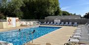 Outdoor swimming pool on a sunny day with two people swimming and lots of empty sun loungers