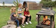 Three children sitting beside a lit outdoor fireplace