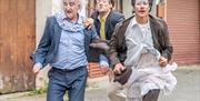 3 clowns running down a street. They seem to be in a race with each other