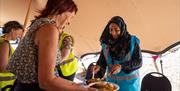A woman serves food to another woman, both smiling.