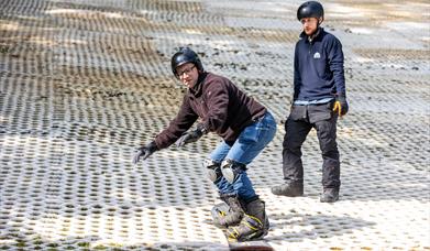 A man having a snowboarding lesson at the Mendip Activity Centre with his instructor looking on