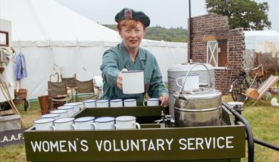 A women in WRVS uniform serving mugs of tea at a Women's Voluntary Service tea stand at a 1940s weekend