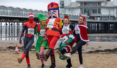 Four runners in festive fancy dress put their best foot forward on the beach in front of the Grand Pier, Weston-super-Mare ahead of the town's annual